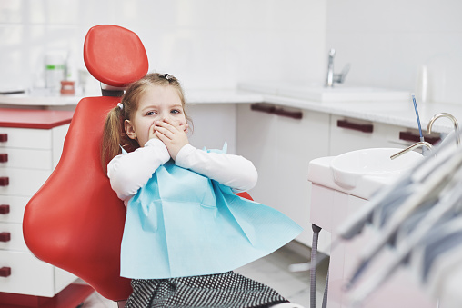 child in dental chair covering mouth