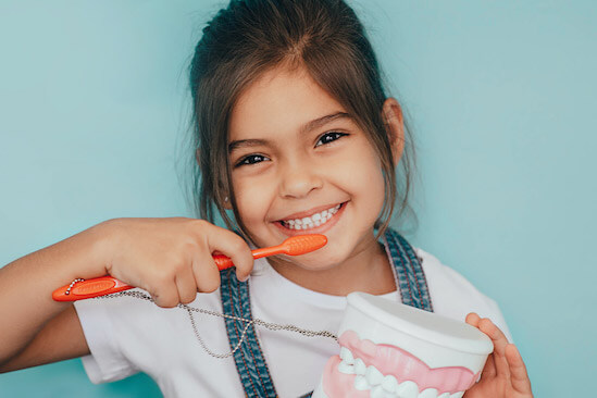 child smiling and holding a toothbrush in front of her teeth to promote brushing that prevent cavities